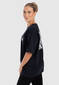 Navyblaues, übergrößes T-Shirt aus Baumwolle mit kurzen Ärmeln, das auf der Rückseite ein weißes Grafikdesign und auf der Vorderseite ein kleines Logo hat.