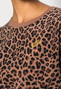 Parte superior de estampado de leopardo marrón con logo de Nike bordado en dorado en el pecho, mostrada en el torso superior y cuello de una persona.