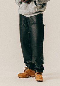 Svarte skinnbukser med løs passform, som har to frontlommer med gullglidelåser. Kombinert med brune semsket støvler med gummisåler.