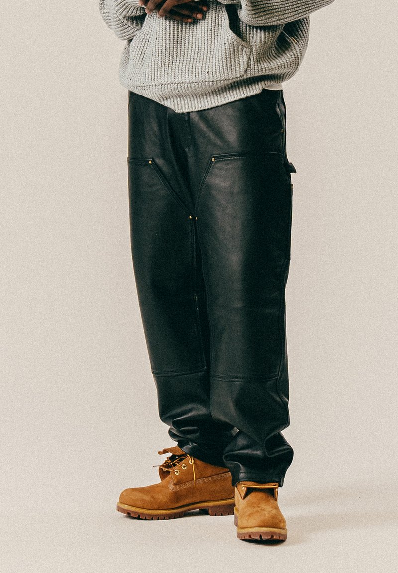 Svarte skinnbukser med løs passform, som har to frontlommer med gullglidelåser. Kombinert med brune semsket støvler med gummisåler.