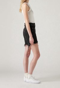 Pantalones cortos de mezclilla negra con dobladillo deshilachado, cintura alta y cinco bolsillos. Combinados con una camiseta sin mangas blanca de canalé y zapatillas blancas.