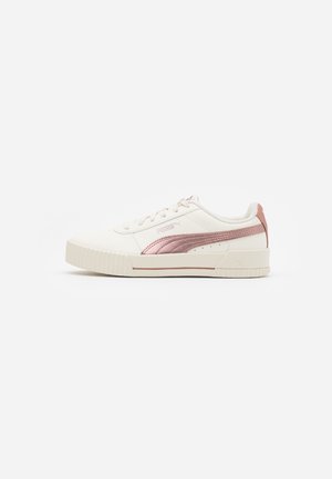 Basket basse blanche avec bande métallique rose Puma, fermeture à lacets et semelle en caoutchouc texturée sur fond uni.