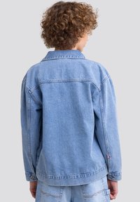 Giacca in denim blu chiaro con collo a punta, maniche lunghe, polsini con bottoni e dettagli di cucitura visibili sulla parte posteriore e sull'orlo.