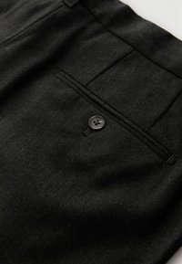 Sorte bukser med fiskebenmønster med en enkelt baglomme med en sort knap, lavet af tekstureret stof.