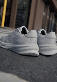 Zapatillas deportivas blancas con un upper texturizado, un talón liso y una suela acolchada. Presentan tres rayas paralelas y sutiles acentos de marca.