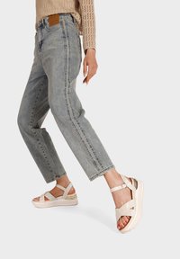 Sandali platform bianchi e beige con cinturini incrociati e dettagli metallici, abbinati a jeans di denim azzurri.