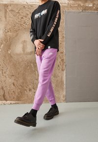 Svart långärmad tröja med färggrafik, parat med ljuslila sweatpants och svarta skor med tjock sula och snörning.