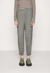 Gray elastic-waist pants with tapered cuffs and side pockets, paired with dark green slip-on shoes, worn over a brown striped long-sleeve top.