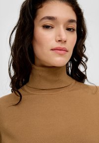 Bruine coltrui gemaakt van zacht materiaal, met een aansluitend ontwerp en een gladde textuur. Minimalistische stijl met een hoge hals.