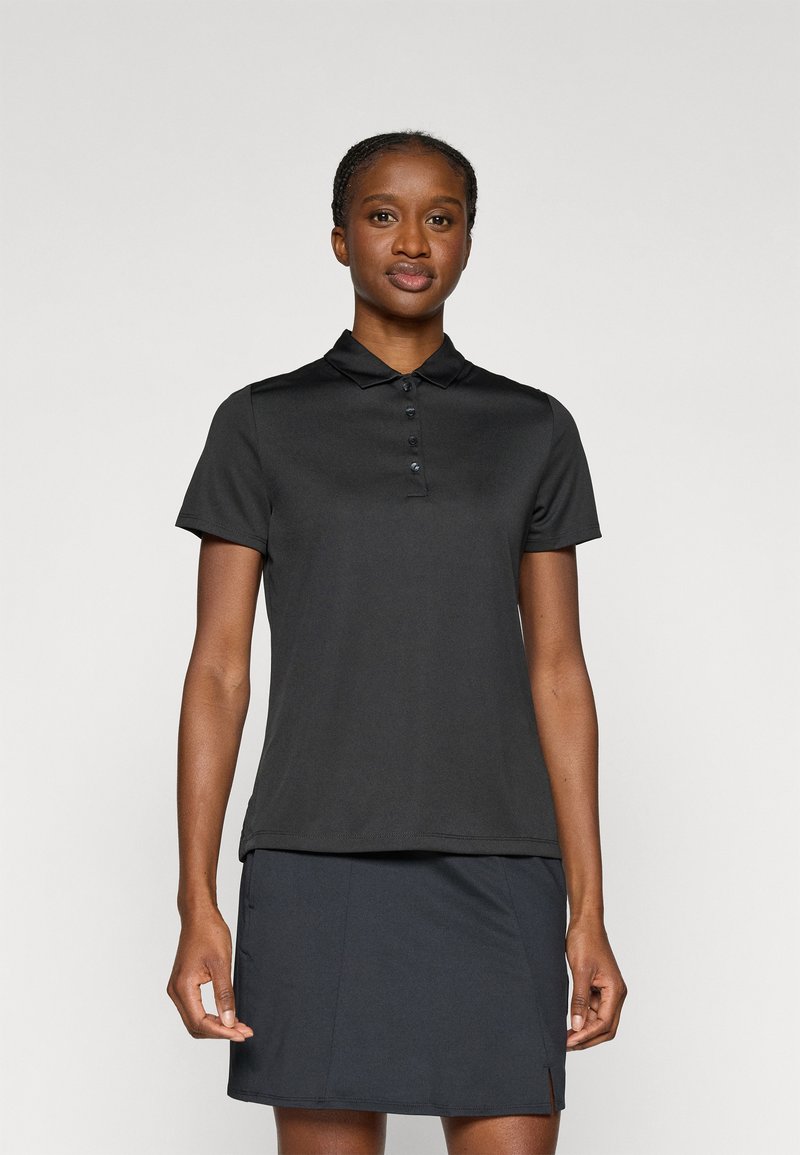 Polo noir à manches courtes, patte de boutonnage, et tissu lisse. Associé à une jupe sombre, les deux avec une coupe ajustée.