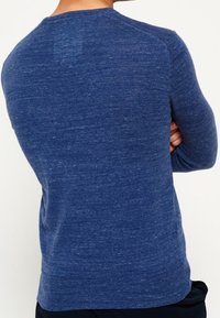 Blau gestrickter Pullover mit strukturierter Oberfläche und langen Ärmeln. Verfügt über einen runden Halsausschnitt und ein tailliertes Design, das eine einfarbige Optik präsentiert.
