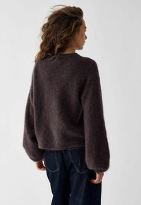 Ciemnofioletowy, puszysty sweter dzianinowy z okrągłym dekoltem i szerokimi rękawami, zestawiony z ciemnoniebieskimi dżinsami. Miękka faktura, skrócony fason.