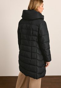 Must muströöp, millel on kõrge krae, koos quilt-kangaga ja keskmise pikkusega disainiga. Seljaosa on puhas ja minimalistlik.