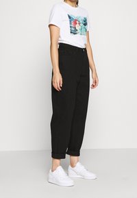 Pantalones ajustados de talle alto negros con un corte relajado y puños enrollados, combinados con una camiseta gráfica blanca y zapatillas blancas.