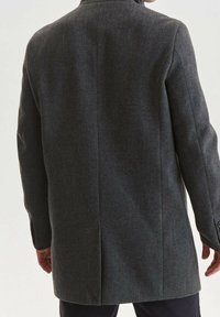 Grauer Fischgrätenmantel aus strukturiertem Stoff, mit einem einzigen Schlitz hinten und geknöpften Ärmeln. Keine weiteren auffälligen Details sichtbar.