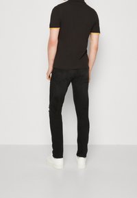 Czarna koszulka polo z krótkim rękawem, z żółtymi i niebieskimi paskami, w połączeniu z czarnymi dżinsami i białymi sneakersami.