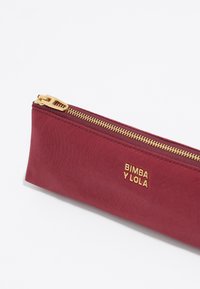 Estuche de lápices burdeos con un acabado texturizado, cremallera dorada y logotipo en relieve. Diseño compacto, forma rectangular, adecuado para el almacenamiento de material de papelería.