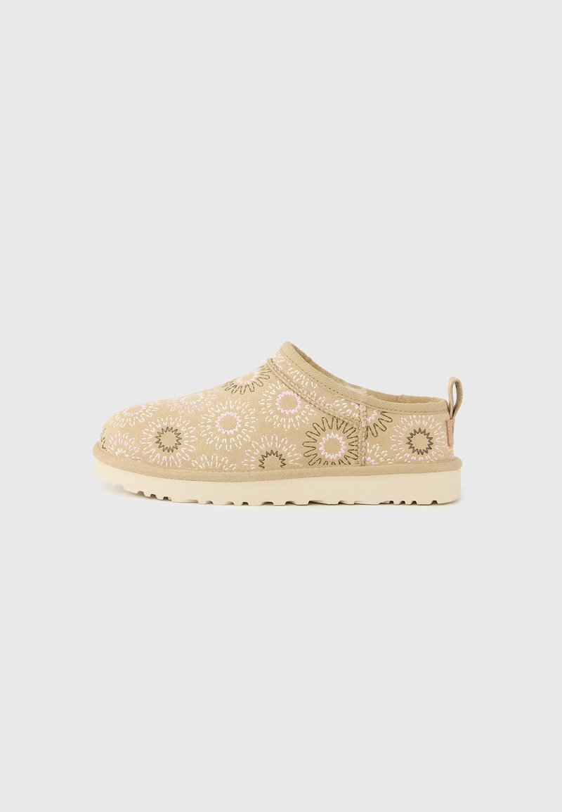 Chausson beige sans lacets avec broderie florale en rose, blanc et vert, doté d'une semelle texturée et d'une languette à l'arrière.