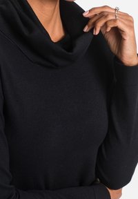 Černý svetr s rolákem, dlouhými rukávy a přiléhavým střihem, vyrobený z měkké, texturované látky. Vyznačuje se výrazným volně padajícím límcem.