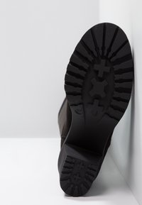 Botte en daim noir avec une semelle extérieure en caoutchouc texturée présentant des rainures profondes pour une meilleure adhérence, vue latérale inclinée mettant en avant un bout arrondi et un design minimaliste.
