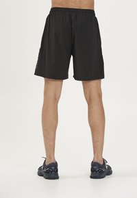 Zwarte sportshorts gemaakt van lichtgewicht materiaal, met een elastische tailleband en een minimaal ontwerp. Enkelhoge hardloopschoenen maken de look compleet.