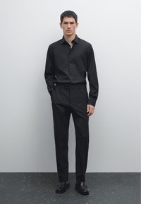 Black dress shirt with button front, long sleeves and fitted design. Paired with black tailored trousers and matching black loafers.