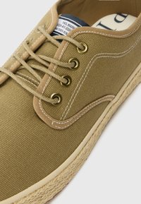 Kanvas-sneaker i khaki med beige detaljer, rund tå, metalløyer og flate snører. Har vevd jute-mellomsåle og kontrastsøm.