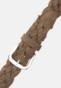 Flätad mockabälte i ljusbrun, med en silvermetallspänne. Texturerad yta med mjuka, fransiga kanter och en smidig stängning.