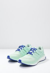 Lekkie buty do biegania w miętowym kolorze, z siateczkową cholewką, niebieskimi sznurowadłami i amortyzowaną podeszwą z teksturowanym wzorem na spodzie.