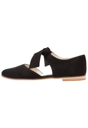 Black suede flats with cut-out sides, tied ankle strap, rounded toe, and a low wooden heel. Smooth inner lining complements the outer texture.