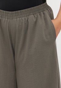 Το παντελόνι έχει ελαστική μέση, χαλαρή εφαρμογή και είναι φτιαγμένο από ελαφρύ, υφασμάτινο υλικό σε μουδιασμένο ελαιοπράσινο χρώμα. Διαθέτει πλαϊνές τσέπες.