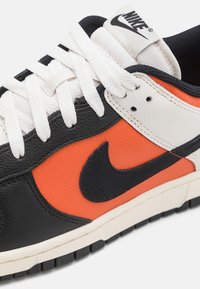 Sneaker Nike con base in pelle nera, sezione centrale arancione, dettagli bianchi, lacci in tessuto, suola nera e logo Swoosh nero ben visibile.