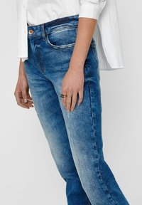 Ljusblå denimjeans med en lätt blekning, slitna detaljer fram, femficksdesign och knappstängning i midjan.