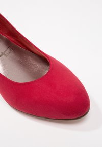 Chaussure plate femme en daim rouge avec bout arrondi et semelle intérieure argentée sur fond blanc.