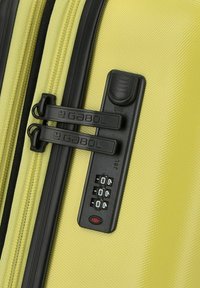 Valigia rigida gialla con chiusure a zip nere e lucchetto a combinazione, caratterizzata da una superficie testurizzata e elementi di design eleganti.