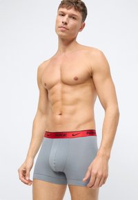 Šedé bavlnené boxerky s červeným pásom s logom Nike, s priliehavým strihom a hladkou textúrou. Žiadne ďalšie doplnky ani vzory.