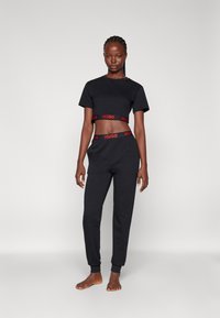 T-shirt noire cropped et pantalon assorti avec une taille "HUGO" rouge. Tissu en coton, manches courtes et poignets côtelés sur le pantalon.
