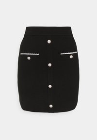 Mini-jupe noire en tissu texturé, avec des boutons semblables à des perles sur le devant et deux poches ornées de bordures blanches.