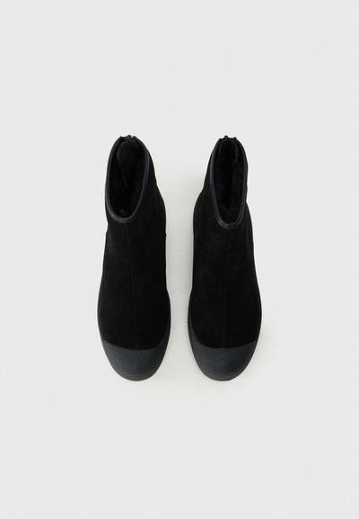 Juodi kulkšniai, pagaminti iš minkštos zomšos, su guminiais pirštų gaubtais. Turi elegantišką dizainą ir lygią vidinę apdailą.