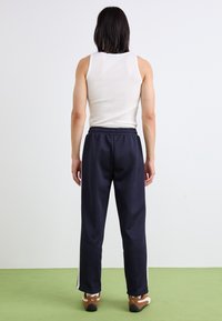 Marinblå joggebukser med elastisk midje og sidelommer, kombinert med en hvit tanktop. Glatt tekstur, avslappet passform og rett ben-design.