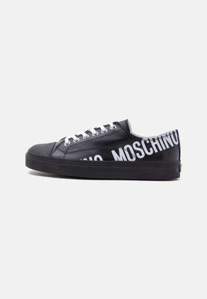 Schwarzer Sneaker mit niedrigem Schnitt, weißen Schnürsenkeln und fett gedrucktem weißen "MOSCHINO"-Text, der um die Ferse und die Seite verläuft.
