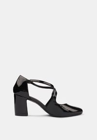 Chaussures à talons hauts en cuir verni noir avec un bout pointu, un talon épais et des brides croisées. Texture lisse avec une finition brillante.