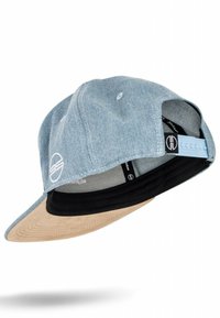 Denim modrá čiapka so svetlohnedým okrajom; má čiernu podšívku a logo na prednej strane. Na zadnej strane je nastaviteľný remienok svetlomodrej farby.