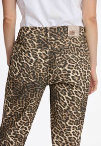 Pantalons à imprimé léopard avec un mélange de teintes beiges et noires, dotés de deux poches arrière et d'une étiquette de marque à la taille.