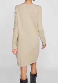 Robe pull en tricot beige avec une coupe décontractée, dotée de manches longues, d'un ourlet côtelé et d'un bas légèrement arrondi. Texture lisse.