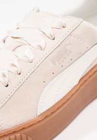 Baskets beige clair en suède avec des accents blancs texturés, dotées de lacets en satin et d'une semelle en caoutchouc de couleur tawny, avec un détail de logo embossé.