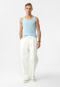 Lichtblauwe tanktop met ronde hals, gecombineerd met witte wijde broeken en neutrale sneakers. Zachte stof met een relaxte pasvorm.