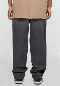 Vaqueros de mezclilla oscuros y holgados con un acabado texturizado y puños elásticos, combinados con una camiseta suelta color beige. Vista desde la parte trasera.