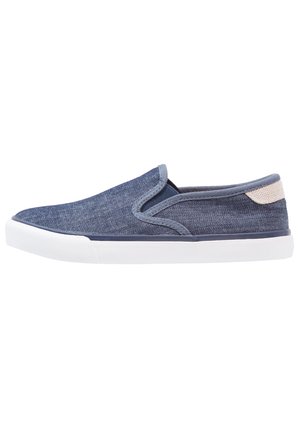 Vapaa-ajan slip-on-tennari sinisestä farkkukankaasta, valkoisella kumipohjalla ja beigenvärisellä kantapäälenkillä, sivuprofiilinäkymä.