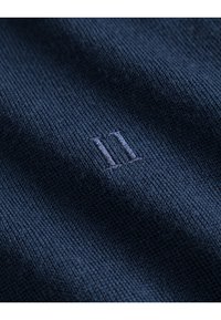 Dunkelblaues Strickgewebe mit einem subtilen strukturierten Muster, verziert mit einer gestickten hellblauen Ziffer "11".